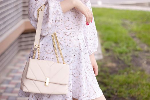 close up of woman in white dress holding fashionable beige purse outside. Product photography. stylish handbag for women.