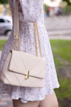 close up of woman in white dress holding fashionable beige purse outside. Product photography. stylish handbag for women.