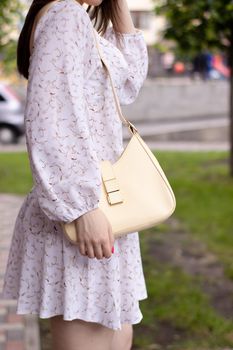 close up of woman in white dress holding fashionable beige purse outside. Product photography. stylish handbag for women.