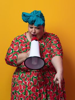 Funny plus size woman posing isolated on yellow background studio portrait. Overweight lady screaming in a megaphone. People emotions lifestyle concept. Mock up copy space. High quality photo