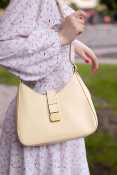 close up of woman in white dress holding fashionable beige purse outside. Product photography. stylish handbag for women.