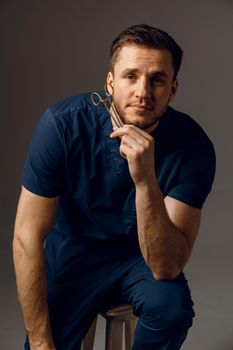 Handsome doctor with surgical scissors close-up. Confident man holding medical equipment in hands and smiling. Happy male posing in studio