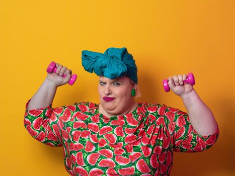 Fat woman dieting, fitness and health at home.Big woman and sport. Healthy, fitness and sports concept. Plus size young woman doing exercise with dumbbells on yellow background. High quality photo