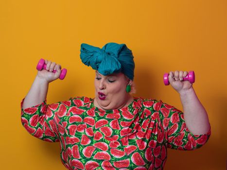 Fat woman dieting, fitness and health at home.Big woman and sport. Healthy, fitness and sports concept. Plus size young woman doing exercise with dumbbells on yellow background. High quality photo