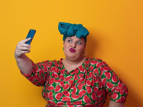 Trendy plus size woman taking selfie photo by smartphone over yellow Fortuna gold background smiling with an idea or question pointing finger with a happy face. High quality photo