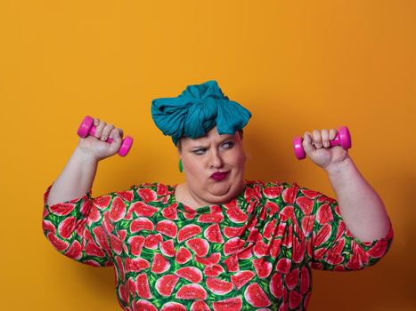 Fat woman dieting, fitness and health at home.Big woman and sport. Healthy, fitness and sports concept. Plus size young woman doing exercise with dumbbells on yellow background. High quality photo