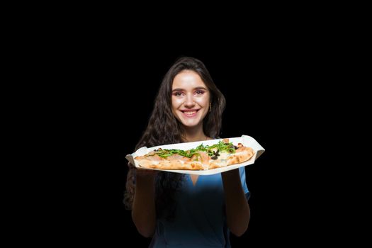 Woman courier with pinsa romana gourmet italian cuisine on black background. Holding scrocchiarella traditional dish. Food delivery from pizzeria. Pinsa with meat, arugula, olives, cheese