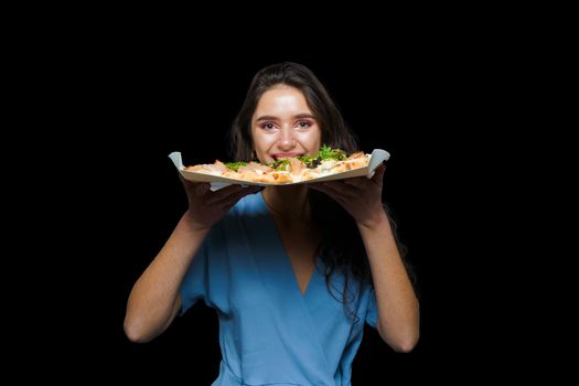 Woman courier with pinsa romana gourmet italian cuisine on black background. Holding scrocchiarella traditional dish. Food delivery from pizzeria. Pinsa with meat, arugula, olives, cheese