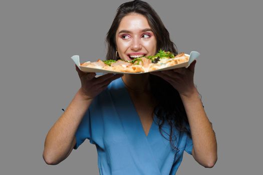 Girl courier with pinsa romana gourmet italian cuisine on gray background. Holding scrocchiarella traditional dish. Food delivery from pizzeria. Pinsa with meat, arugula, olives, cheese