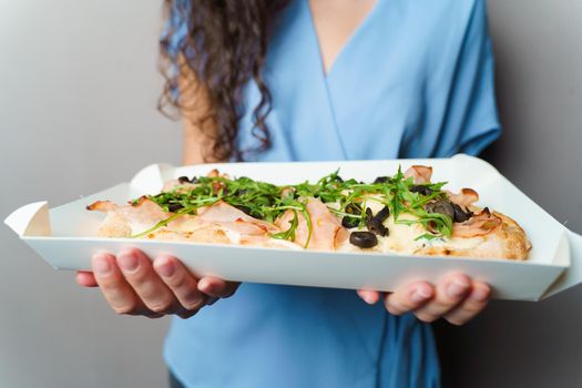 Pinsa romana in white delivery box. Courier holding crocchiarella gourmet italian cuisine on white background. Food delivery from pizzeria. Pinsa with meat, arugula, olives, cheese