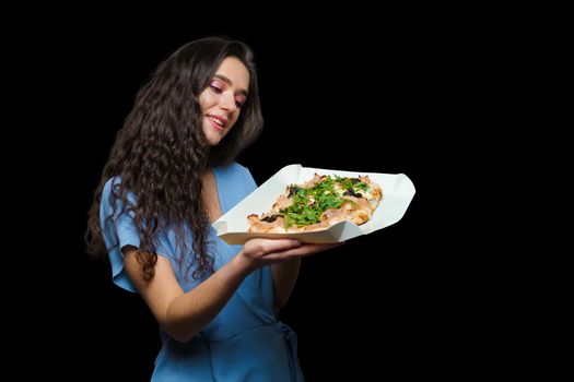 Woman courier with pinsa romana gourmet italian cuisine on black background. Holding scrocchiarella traditional dish. Food delivery from pizzeria. Pinsa with meat, arugula, olives, cheese