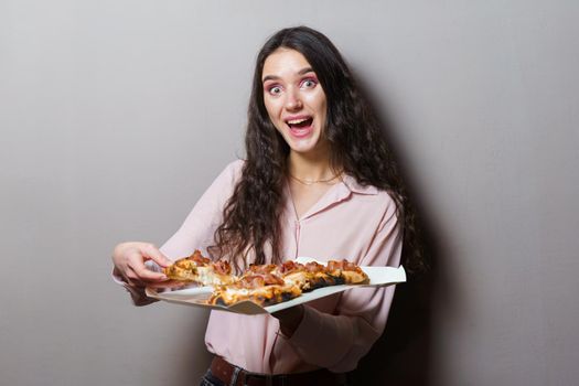 Girl courier with pinsa romana gourmet italian cuisine on grey background. Holding scrocchiarella traditional dish. Food delivery from pizzeria. Pinsa with meat, arugula, olives, cheese.