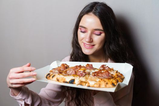 Girl courier with pinsa romana gourmet italian cuisine on grey background. Holding scrocchiarella traditional dish. Food delivery from pizzeria. Pinsa with meat, arugula, olives, cheese.