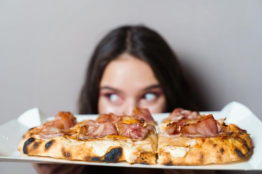 Girl courier with pinsa romana gourmet italian cuisine on grey background. Holding scrocchiarella traditional dish. Food delivery from pizzeria. Pinsa with meat, arugula, olives, cheese.