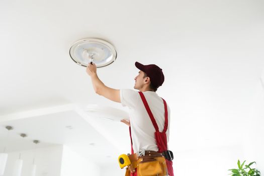 Electrician installs a chandelier on the ceiling. Construction concept.