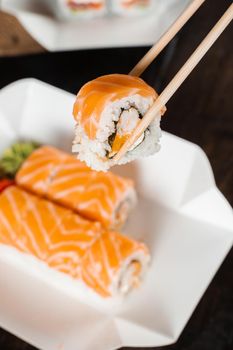 Holding philadelphia roll using chopstics for sushi. Roll with salmon, shrimp and mango. Japanese food delivery