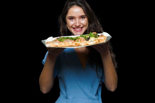 Woman courier with pinsa romana gourmet italian cuisine on black background. Holding scrocchiarella traditional dish. Food delivery from pizzeria. Pinsa with meat, arugula, olives, cheese