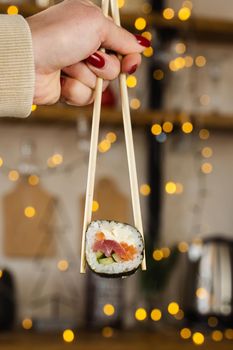 Holding sushi roll on the new year lights background. Christmas decoration. Food delivery at new year eve. Roll with salmon, tuna, cucumber and soft cheese