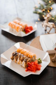 Sushi rolls on the new year lights background. Christmas decoration. Food delivery at new year eve. Roll with salmon, tuna, cucumber and soft cheese