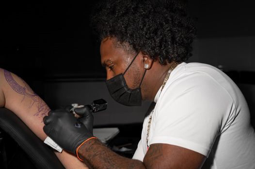 Professional African American tattoo artist makes a tattoo on client arm. High quality photography.