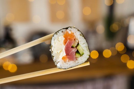 Holding sushi roll on the new year lights background. Christmas decoration. Food delivery at new year eve. Roll with salmon, tuna, cucumber and soft cheese