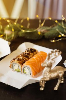 Sushi roll on the new year lights background. Christmas lights decoration. Food delivery at new year eve. Roll with salmon, eel, avocado and soft cheese