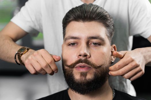 Fixing the shape of mustache with wax. The result of a haircut in a barbershop