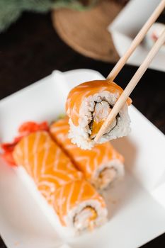 Holding philadelphia roll using chopstics for sushi. Roll with salmon, shrimp and mango. Japanese food delivery