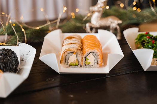 Sushi roll on the new year lights background. Christmas lights decoration. Food delivery at new year eve. Roll with salmon, eel, avocado and soft cheese