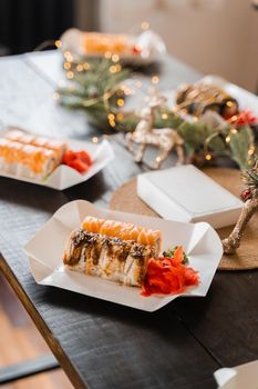 Sushi rolls on the new year lights background. Christmas decoration. Food delivery at new year eve. Roll with salmon, tuna, cucumber and soft cheese