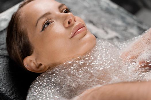 Close-up portrait of girl on foam peeling procedures in spa. Model is relaxing in Turkish hammam