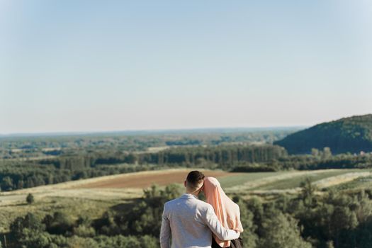 Muslim love story. Mixed couple smiles and hugs on the green hills . Woman weared in hijab looks to her man. Advert for on-line dating agency