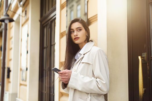 A woman on the street uses a mobile phone. online shopping. use of mobile applications. beautiful woman with long dark hair in a raincoat