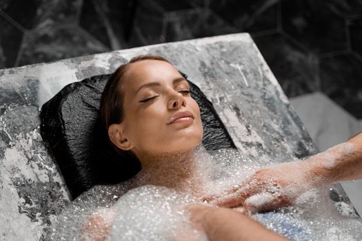 Close-up portrait of girl on foam peeling procedures in spa. Model is relaxing in Turkish hammam