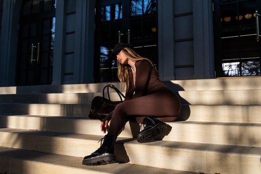 Fashionable young brunette woman with long legs. wearing solid long sleeve bodycon one piece jumpsuits posing with a leather brown travel bag on city street in old town