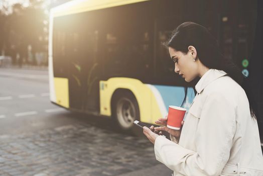 A woman on the street uses a mobile phone. online shopping. use of mobile applications. beautiful woman with long dark hair in a raincoat