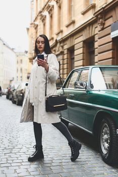 A woman on the street uses a mobile phone. online shopping. use of mobile applications. beautiful woman with long dark hair in a raincoat