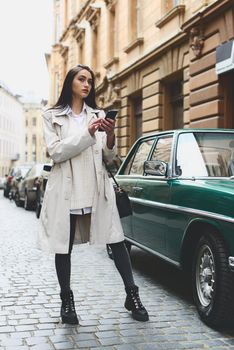 A woman on the street uses a mobile phone. online shopping. use of mobile applications. beautiful woman with long dark hair in a raincoat