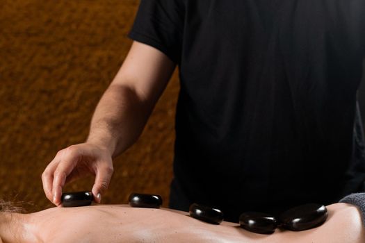Masseur placed hot stone on the back of woman. Manual therapy in spa
