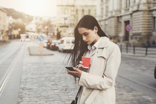 A woman on the street uses a mobile phone. online shopping. use of mobile applications. beautiful woman with long dark hair in a raincoat