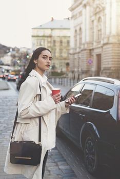 A woman on the street uses a mobile phone. online shopping. use of mobile applications. beautiful woman with long dark hair in a raincoat