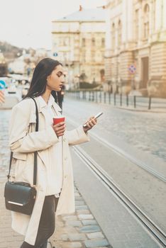 A woman on the street uses a mobile phone. online shopping. use of mobile applications. beautiful woman with long dark hair in a raincoat