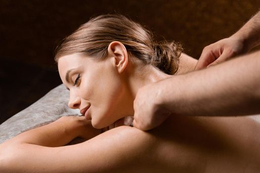 Attractive girl is relaxing on classic massage procedure in spa. Manual therapy. Masseur is doing shoulder massage