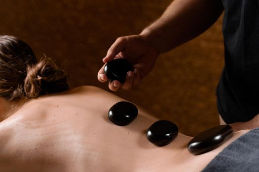 Heated stones on back of woman. Stone massage therapy in spa for relaxing