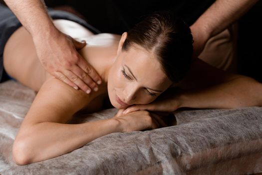 Attractive girl is relaxing on classic massage procedure in spa. Manual therapy. Masseur is doing shoulder massage