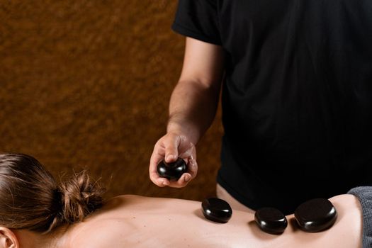Heated stones on back of woman. Stone massage therapy in spa for relaxing