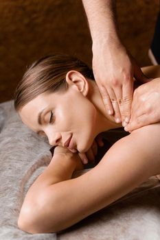 Attractive girl is relaxing on classic massage procedure in spa. Manual therapy. Masseur is doing shoulder massage