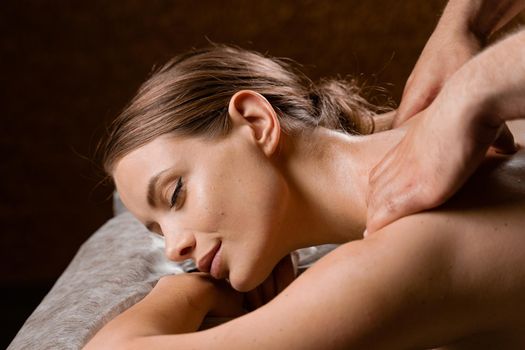 Attractive girl is relaxing on classic massage procedure in spa. Manual therapy. Masseur is doing shoulder massage