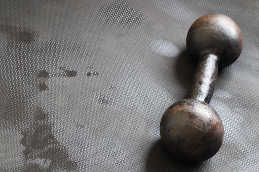 Iron dumbbell training weight on sweaty wet gym exercise mat after workout