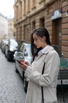 A woman on the street uses a mobile phone. online shopping. use of mobile applications. beautiful woman with long dark hair in a raincoat